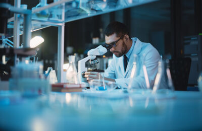 Medical Development Laboratory: Caucasian Female Scientist Looking Under Microscope, Analyzes Petri Dish Sample. Specialists Working on Medicine, Biotechnology Research in Advanced Pharma Lab